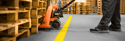 Un transpalette en action dans un entrepôt équipé de dalles PVC Fortelock.  Ces dalles robustes supportent facilement les charges lourdes et le trafic intense.
