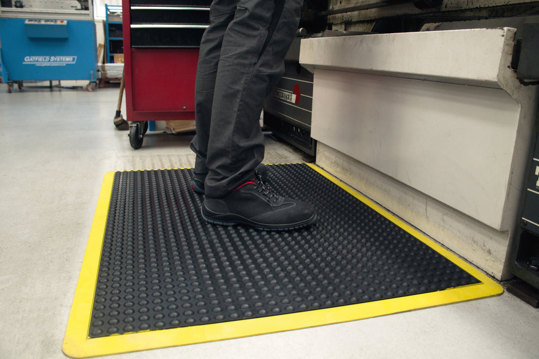 Opérateur debout sur un tapis anti-fatigue à bulles à bords jaunes, devant son poste de travail