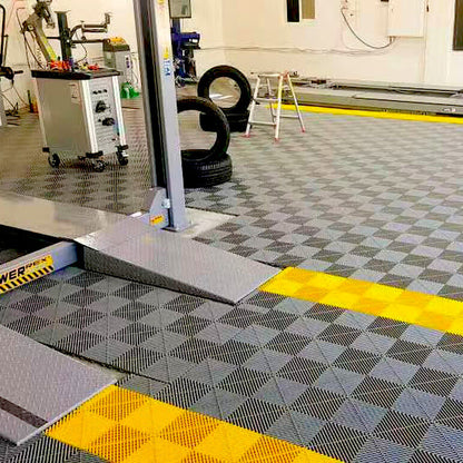 Dalles perforées AERO grises et jaunes sous un pont élévateur de garage